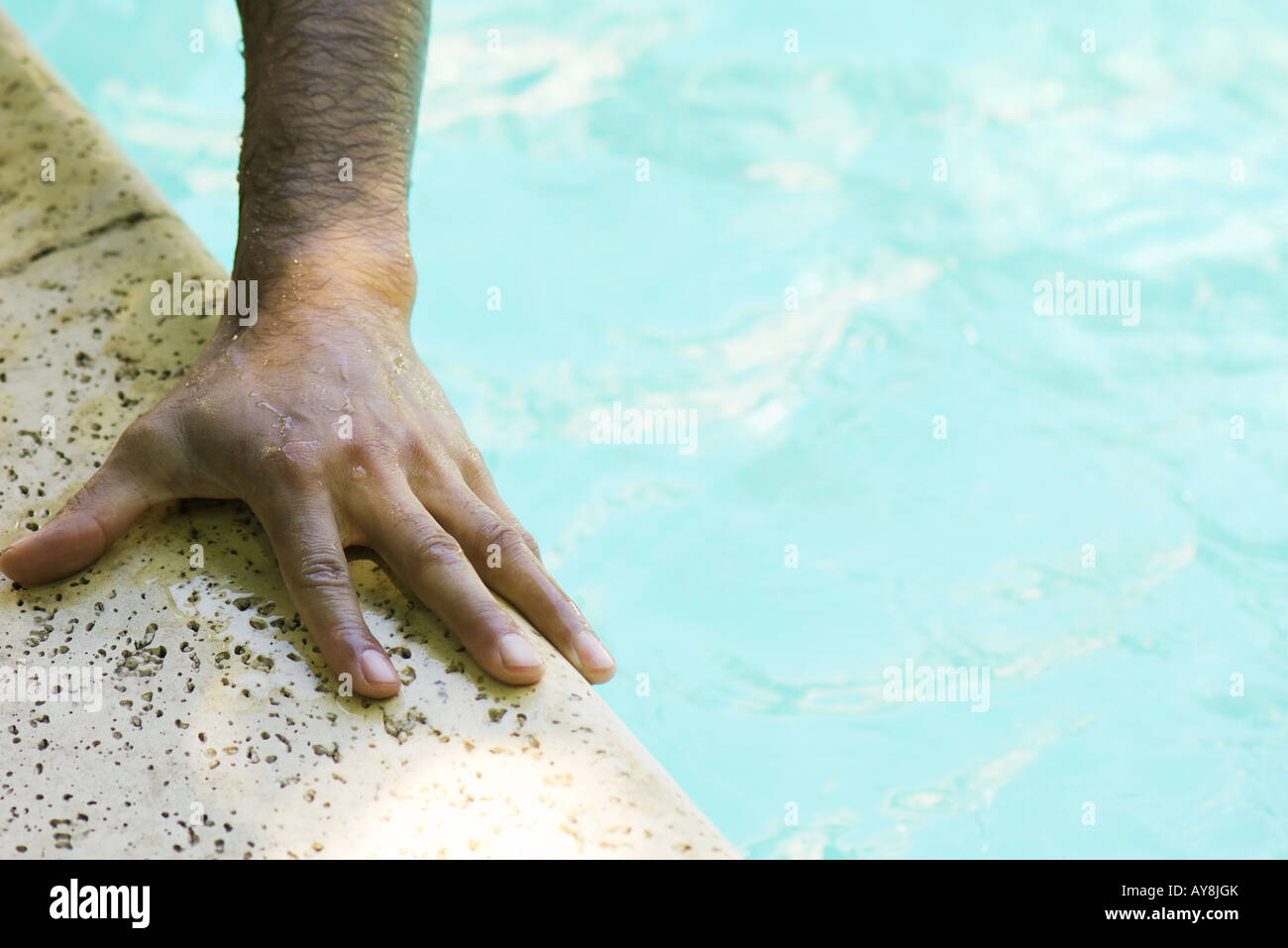 Man's hand holding side of swimming pool, close-up, cropped Stock Photo