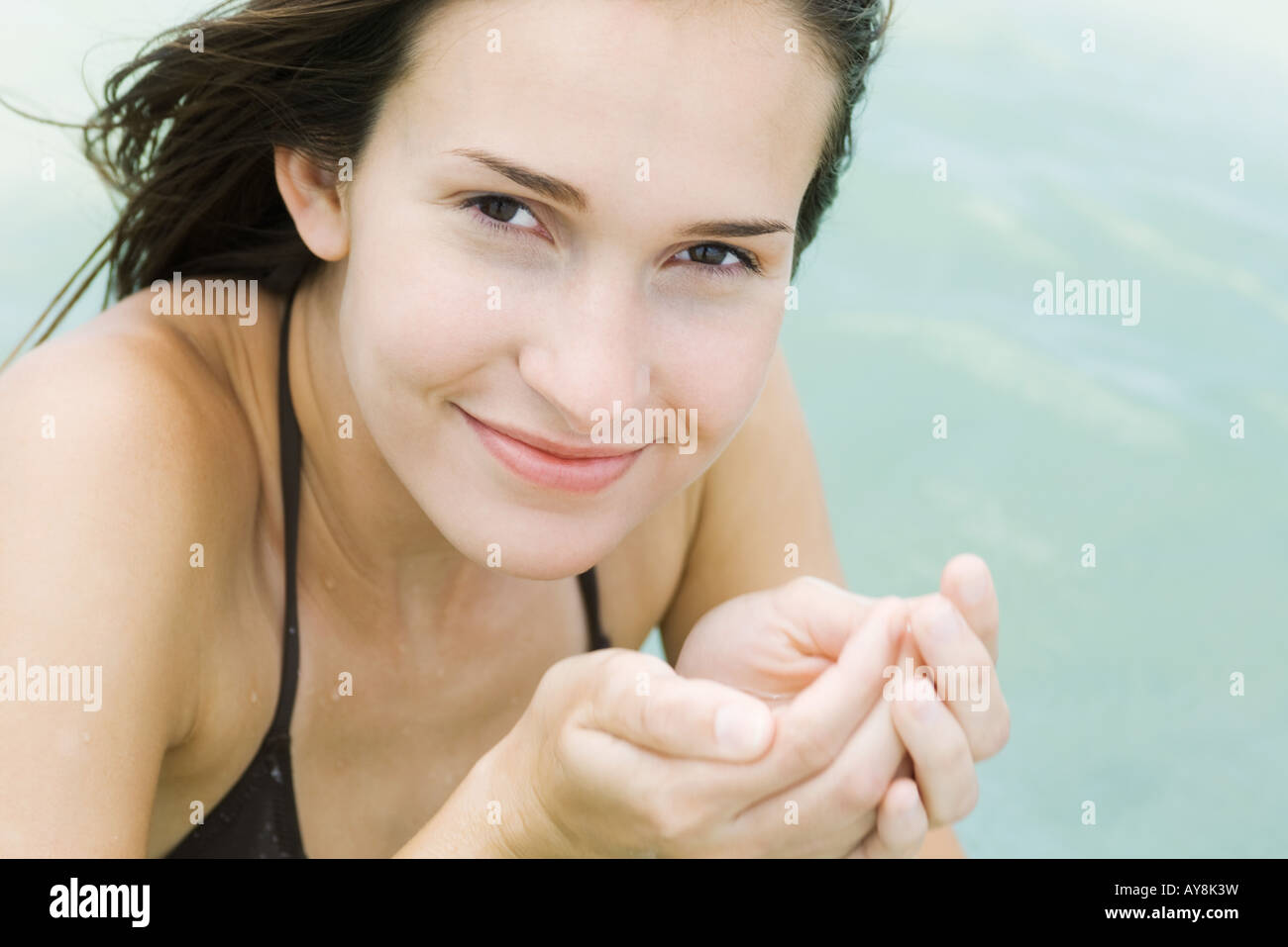 Young woman holding water in cupped hands, smiling at camera, close-up Stock Photo