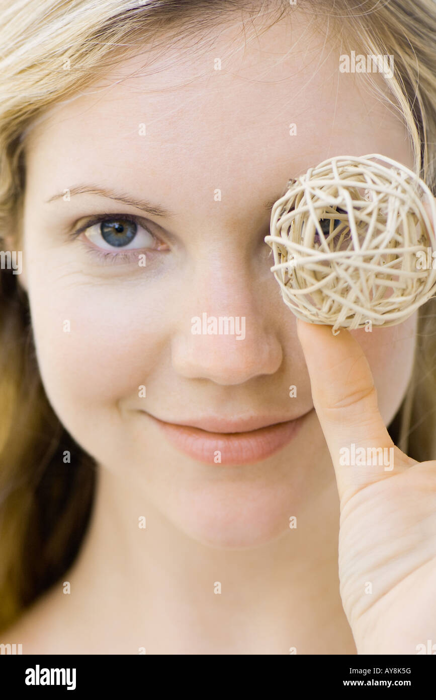 Young woman holding ball in front of one eye, smiling at camera, portrait Stock Photo