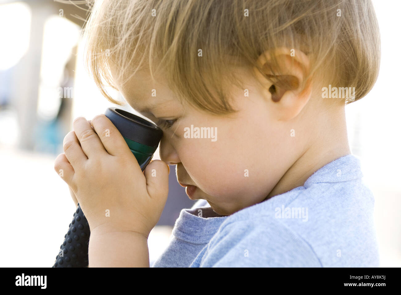 Child holding flashlight against face, side view, closeup Stock Photo