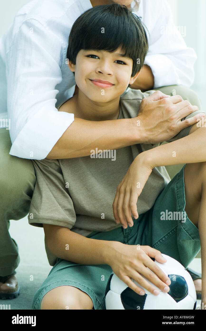 Boy crouching in front of father, holding soccer ball, smiling at camera Stock Photo