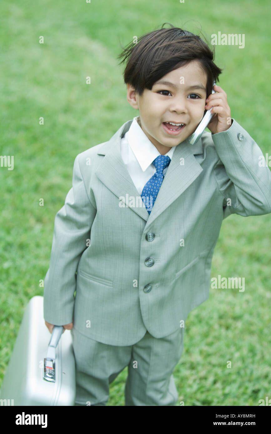 Young boy dressed in suit, using cell phone, carrying briefcase Stock