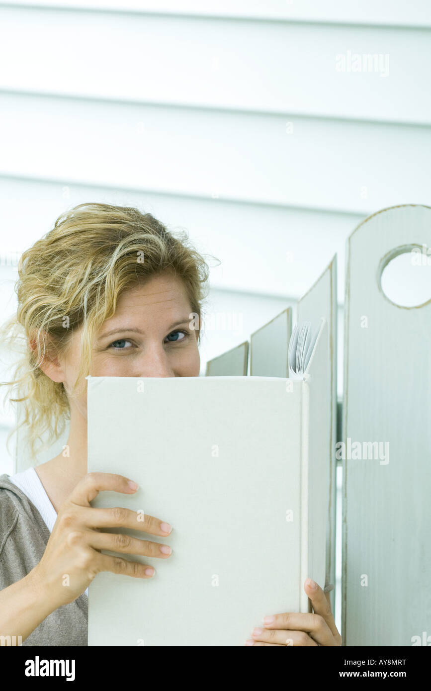 Woman looking over book at camera, close-up Stock Photo