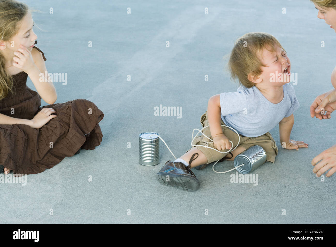 Little boy holding tin can phone, having tantrum, mother and sister watching Stock Photo