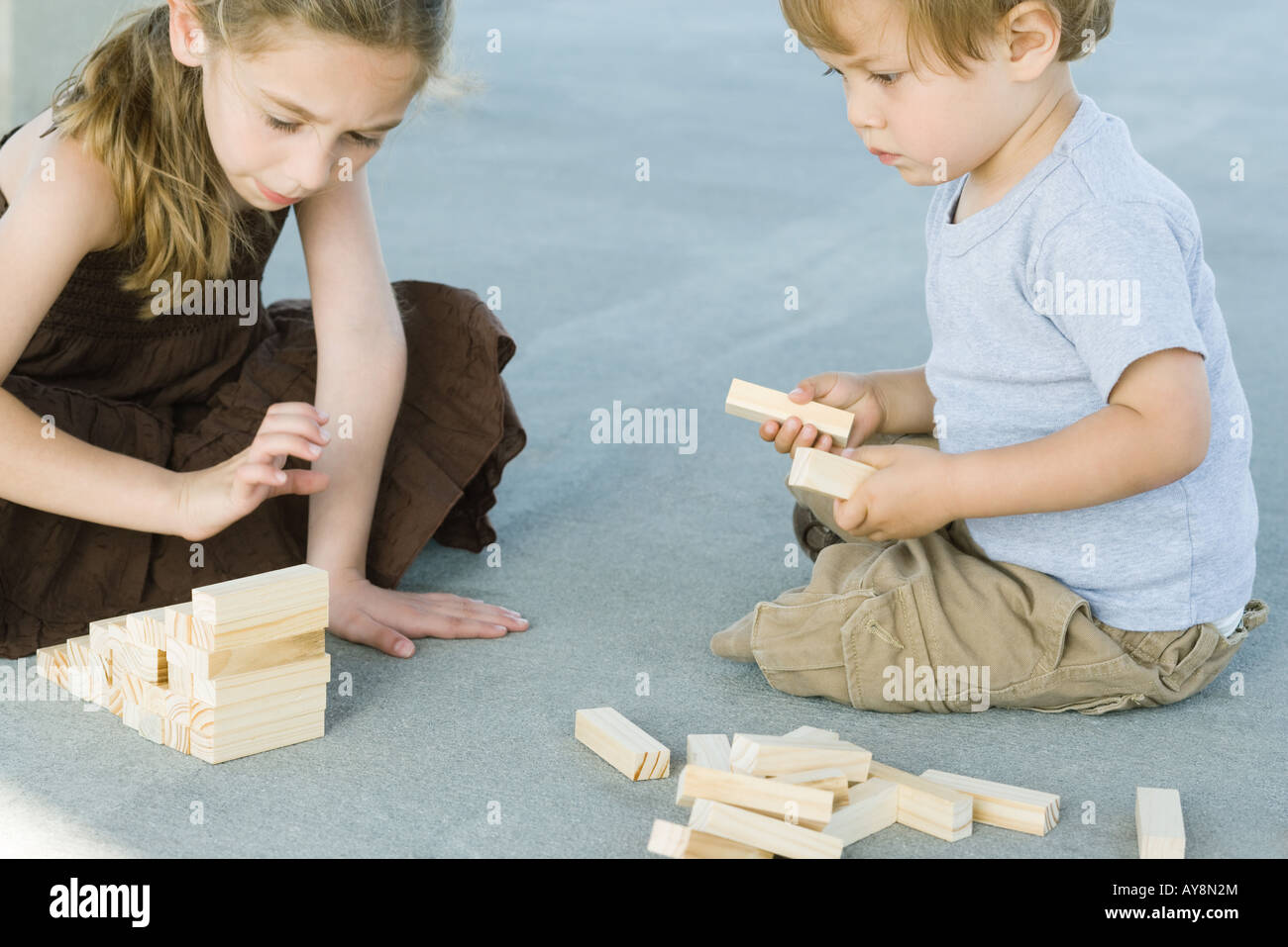 Brother and sister sitting on the ground, playing with building blocks together Stock Photo