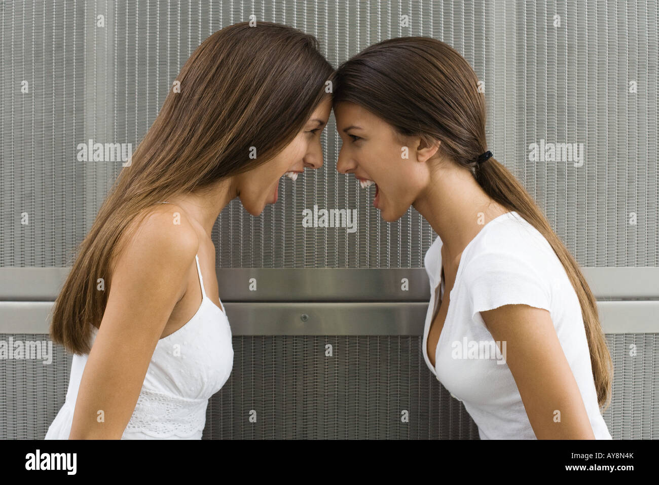 Teenage twin sisters leaning with foreheads touching, both shouting, side view Stock Photo