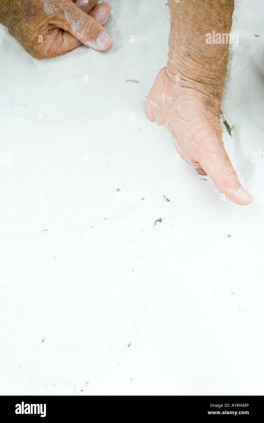 Man with hand half-buried in sand, cropped view, close-up Stock Photo