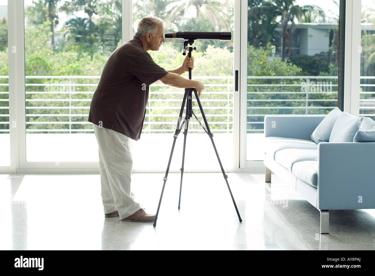 Man standing in living room, looking through telescope, side view Stock