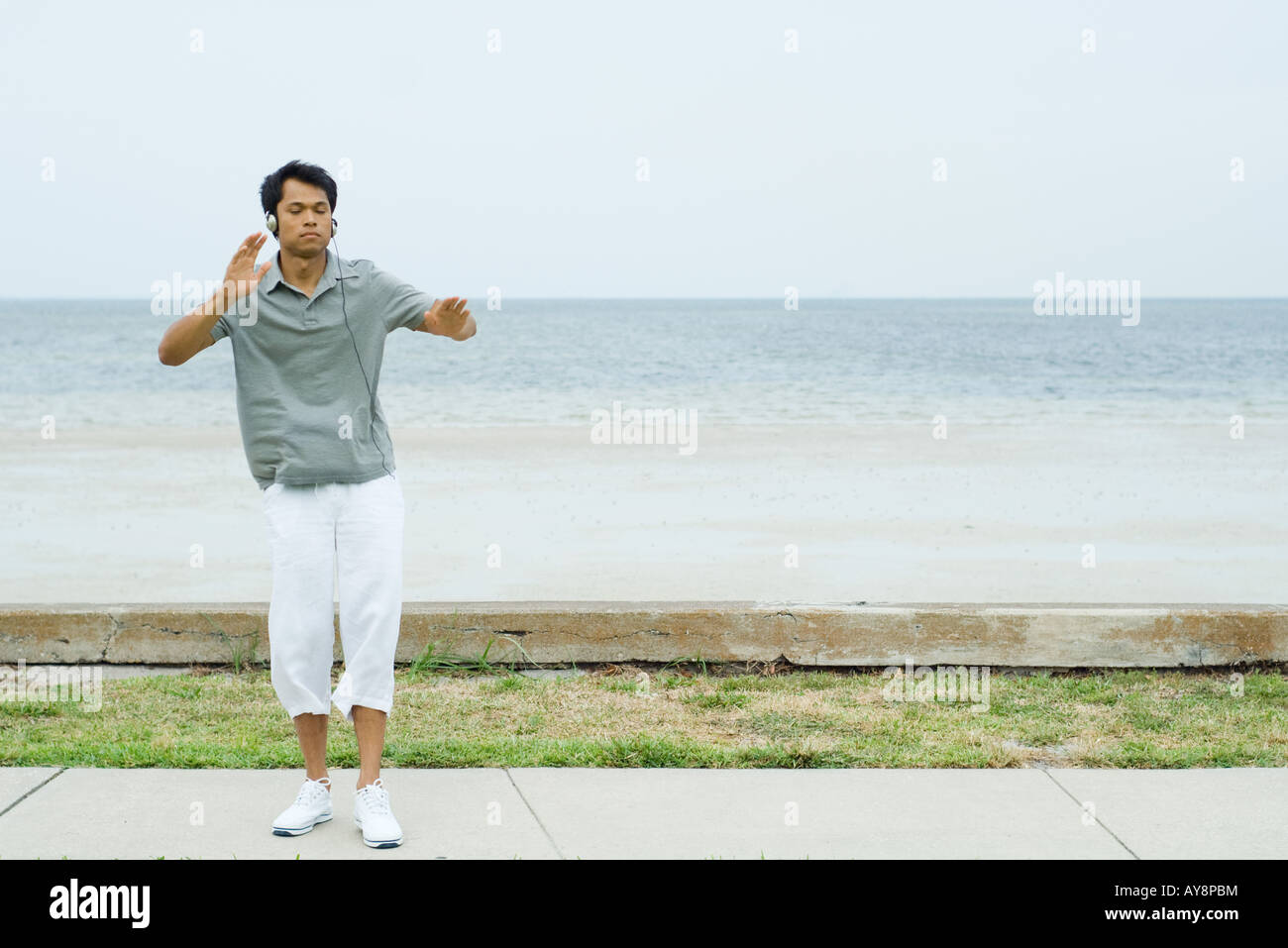 Man standing at the beach with arms out, listening to headphones, eyes closed Stock Photo