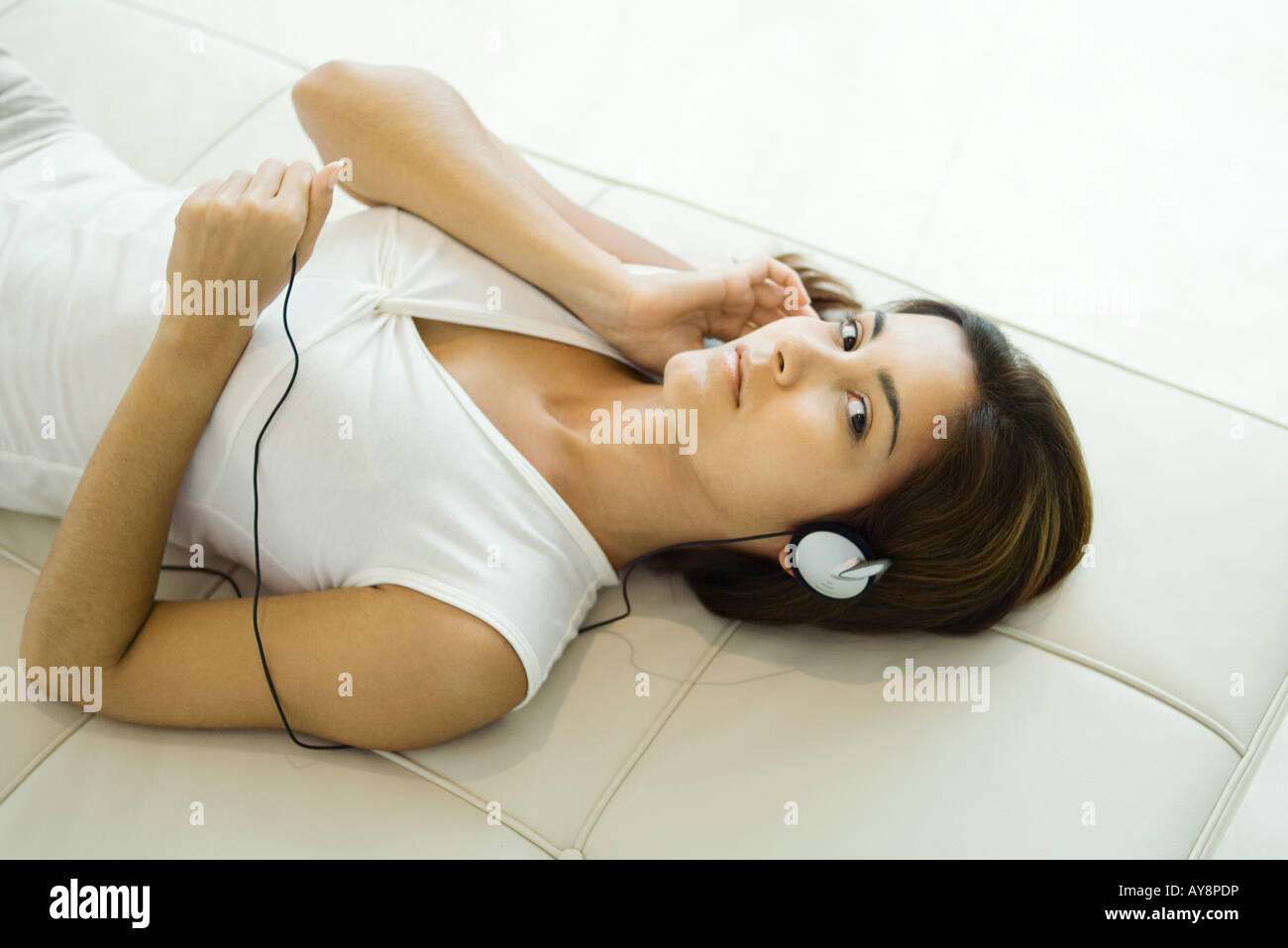 Woman lying on back, listening to headphones, looking at camera, high angle view Stock Photo