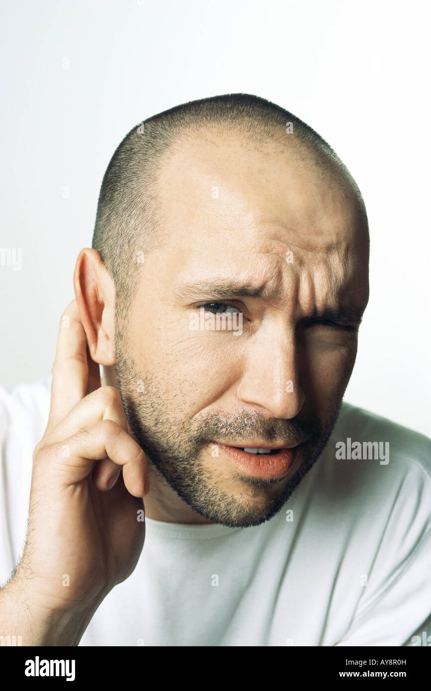 Man holding ear, furrowing brow, looking at camera, close-up Stock Photo