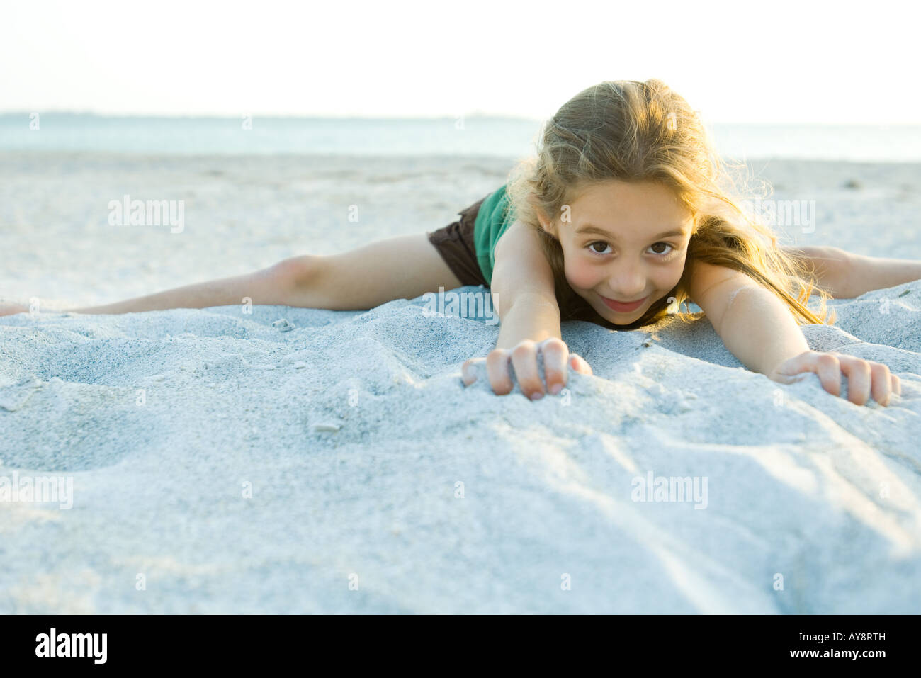 Little girl lying in sand at the beach, smiling at camera Stock Photo