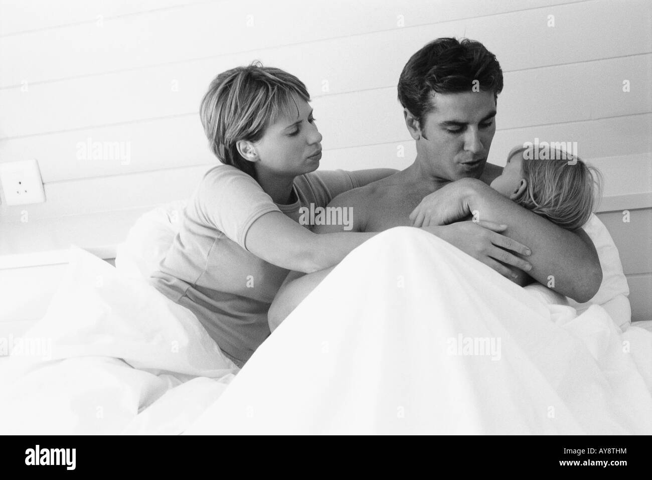 Couple lying in bed, man holding child in arms Stock Photo