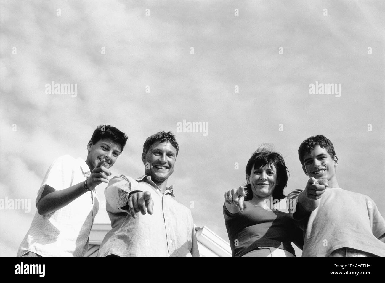Family standing together outdoors, pointing and smiling at camera, low angle view Stock Photo