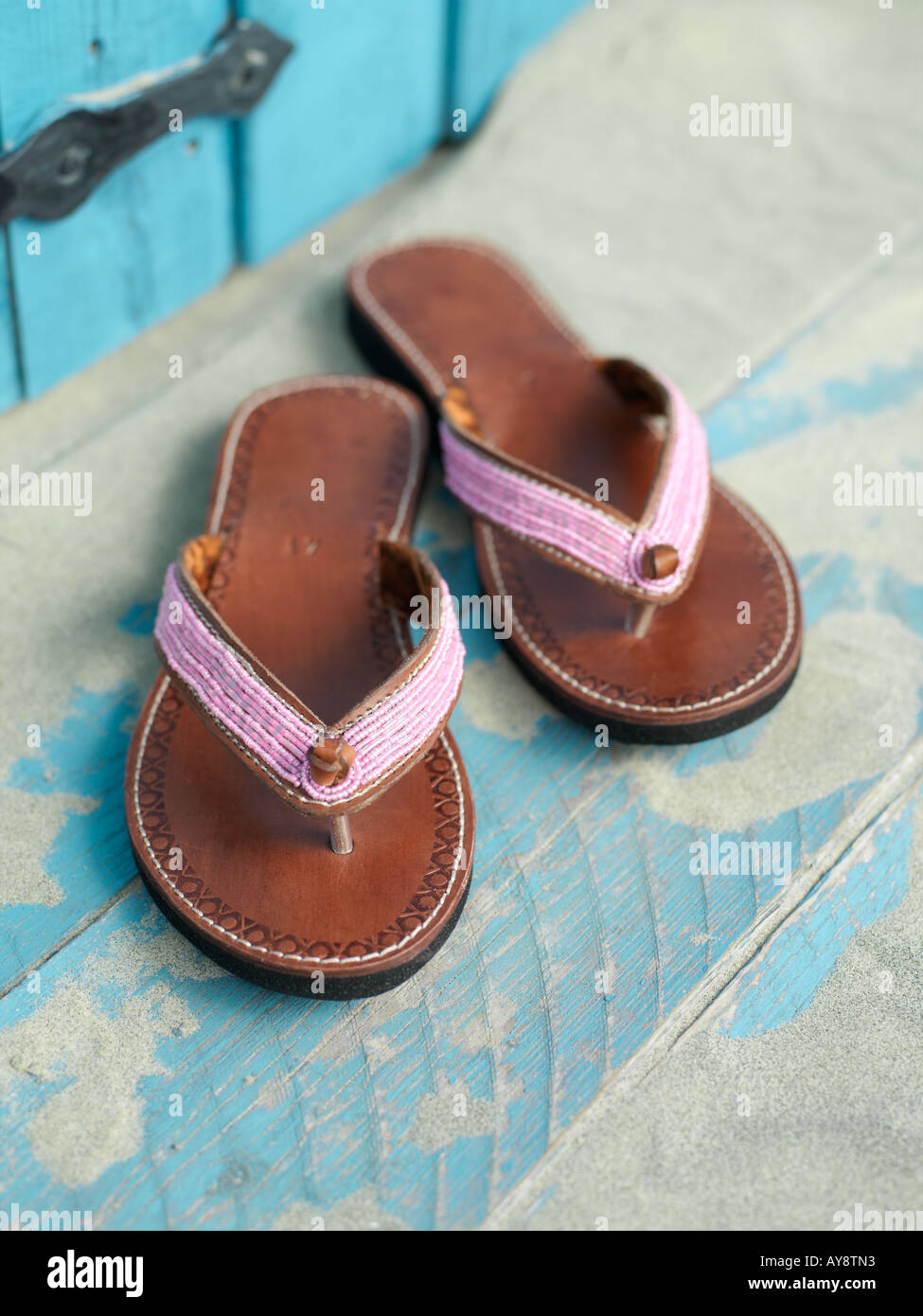 Pair of pink beaded leather summer sandals on a sandy wooden floor Stock Photo