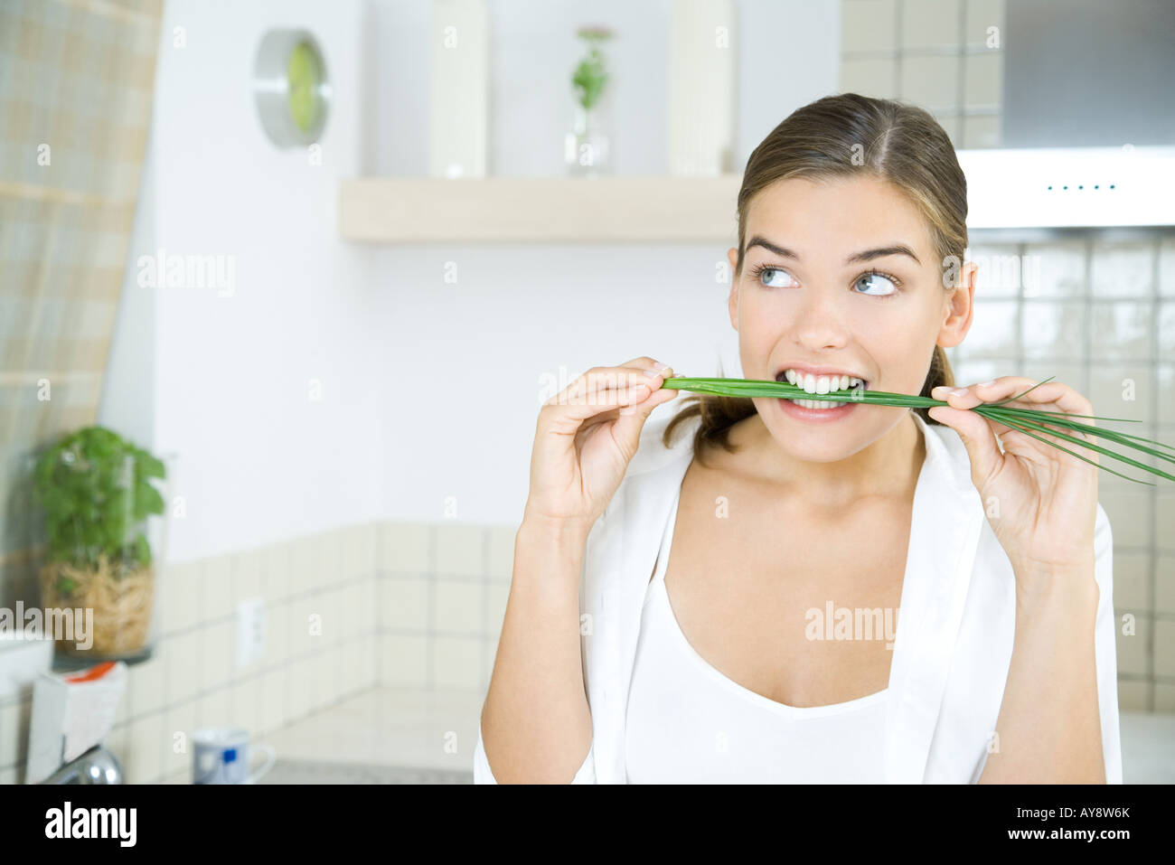 Woman in kitchen, biting into fresh chives, looking away Stock Photo