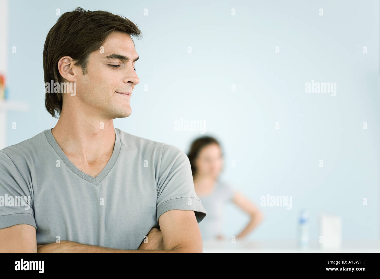 Man with arms folded, looking away, woman standing in background Stock Photo