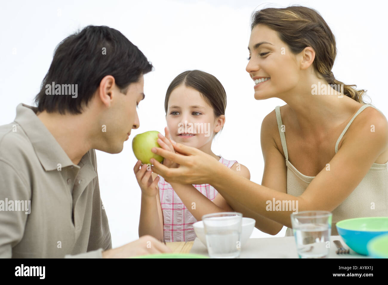 Family of healthy eaters, mother and daughter holding apple toward father Stock Photo