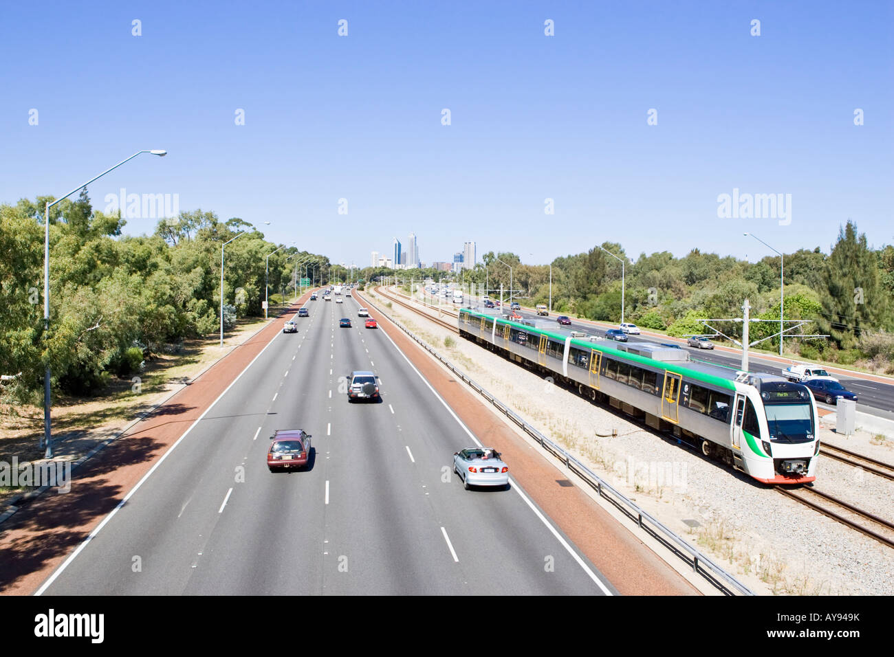 A Transperth electric train heading towards Perth city next to the Mitchell Freeway, Leederville.Skyscrapers are in the distance Stock Photo