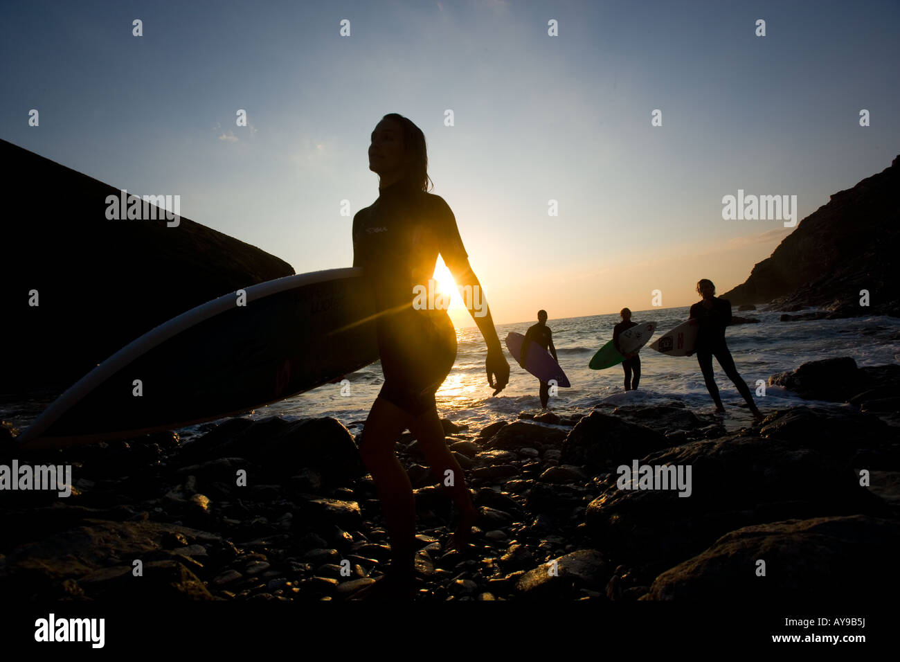 Surfers with boards at waters edge, sunset in Cornwall Stock Photo