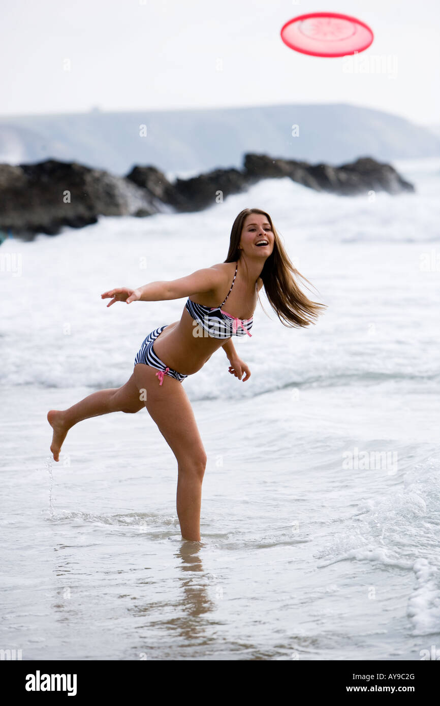 Woman in bikini throwing Frisbee at waters edge, Cornwall, UK Stock Photo