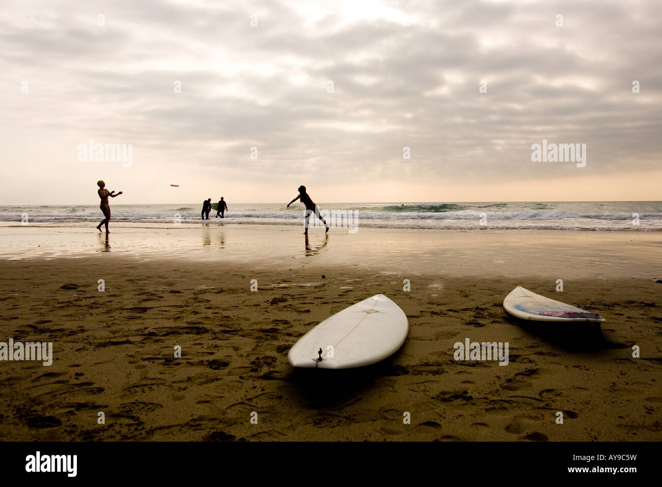 Surfboards at waters edge with people playing Frisbee, Chapel Porth, Cornwall, UK Stock Photo