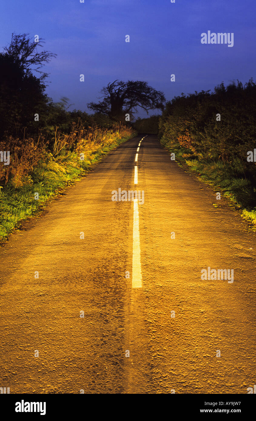 vehicle headlights shining down country road at dusk leeds yorkshire uk Stock Photo