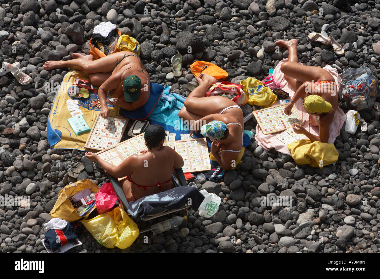 Four Spanish women playing cards and bingo on rocky beach in front of their houses on Gran Canaria Stock Photo