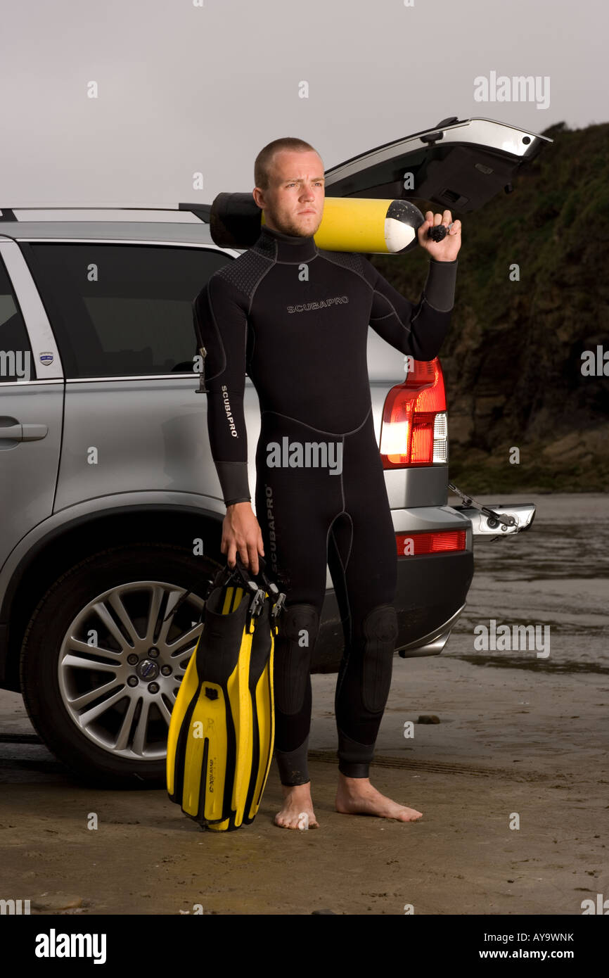 Scuba diver standing with tank and flippers beside car on beach Stock Photo