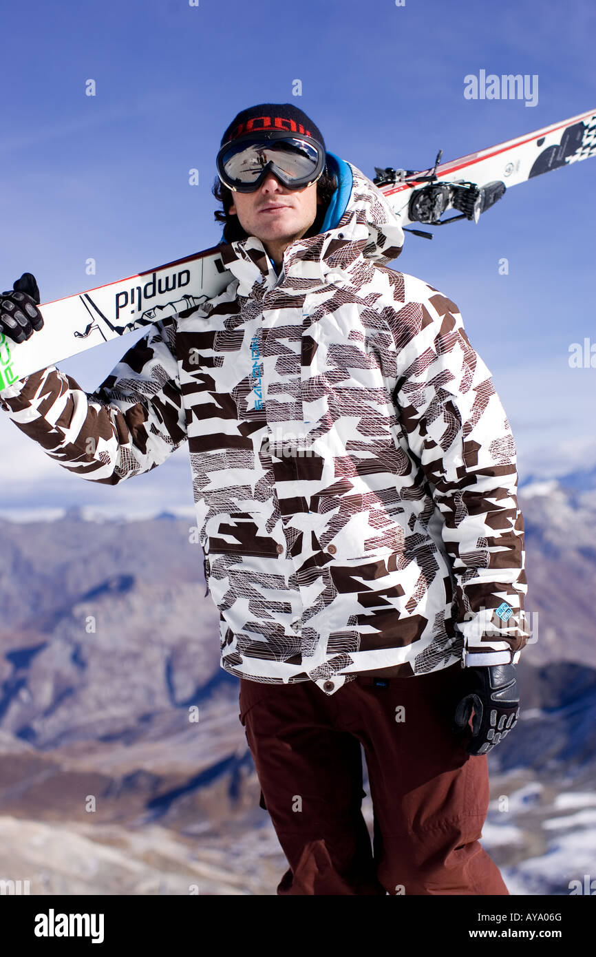 Skier standing in patterned jacket with skis on shoulders, Tignes France Stock Photo