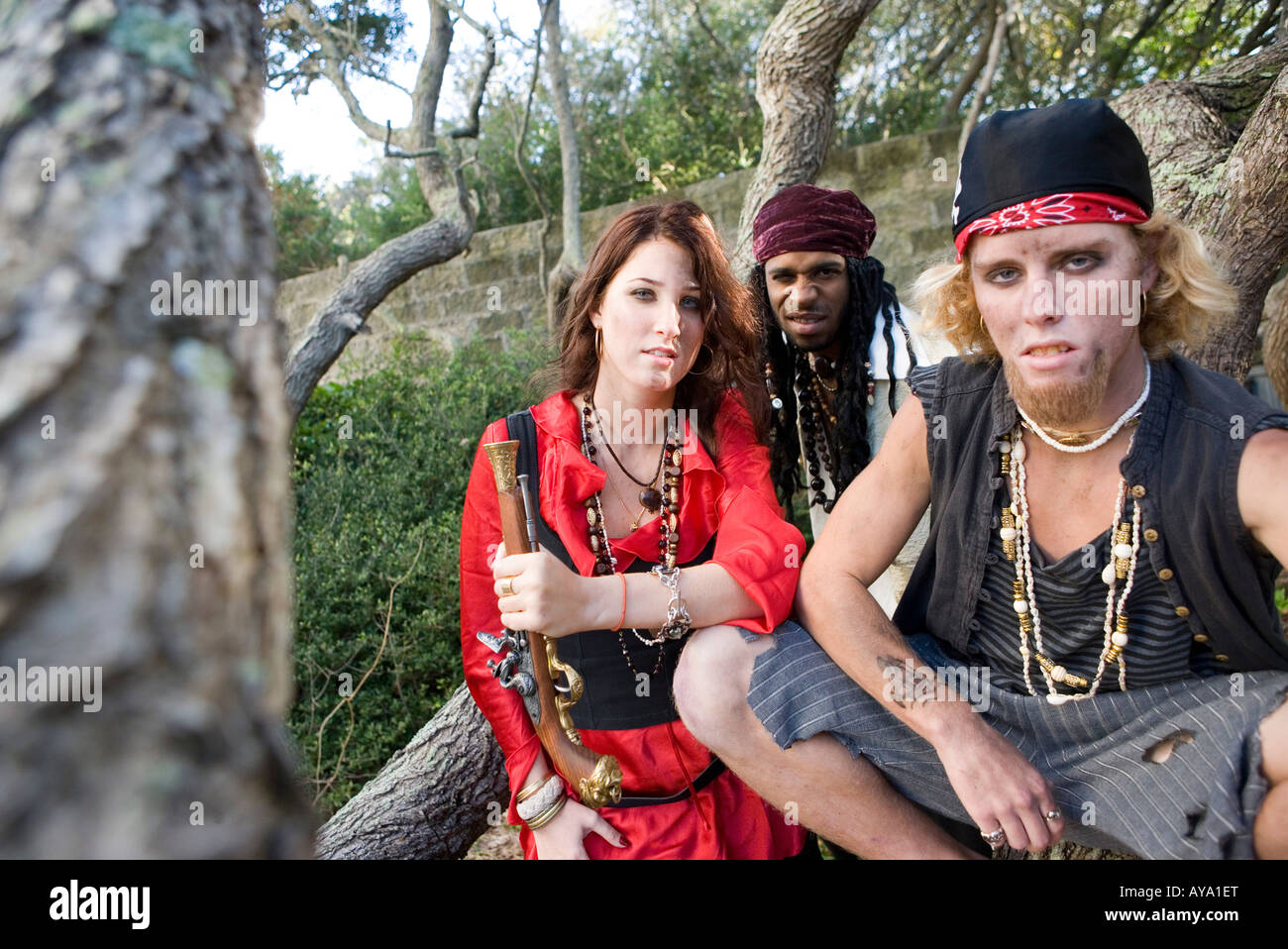 Portrait of pirates sitting under trees with woman pirate holding a gun Stock Photo