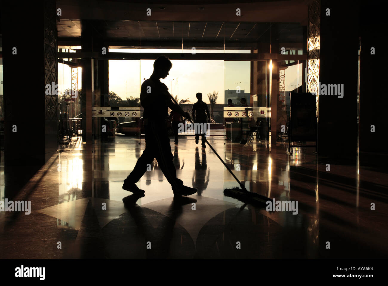 Indonesia Jakarta Silhouette of man pushing broom cleaning floor inside shopping mall Stock Photo