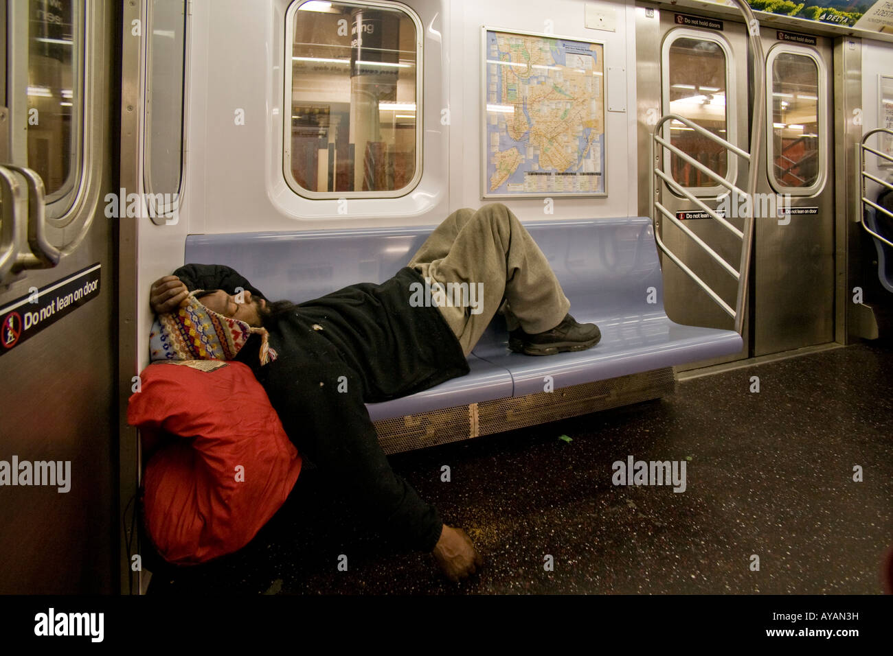 A homeless man sleeps on a subway seat in New York City Stock Photo