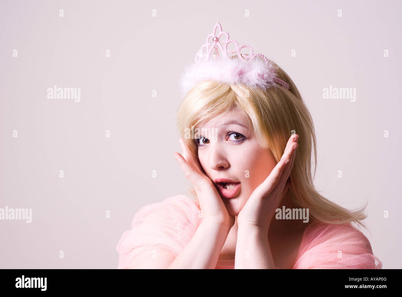 Surprised beautiful woman wearing pink tiara hands on face mouth open looking at camera Stock Photo