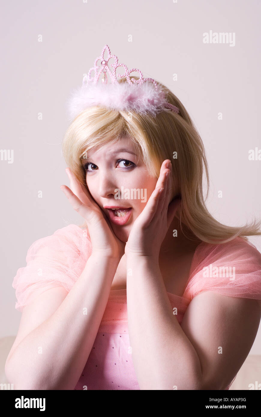 Surprised beautiful woman wearing pink tiara hands on face mouth open looking at camera Stock Photo