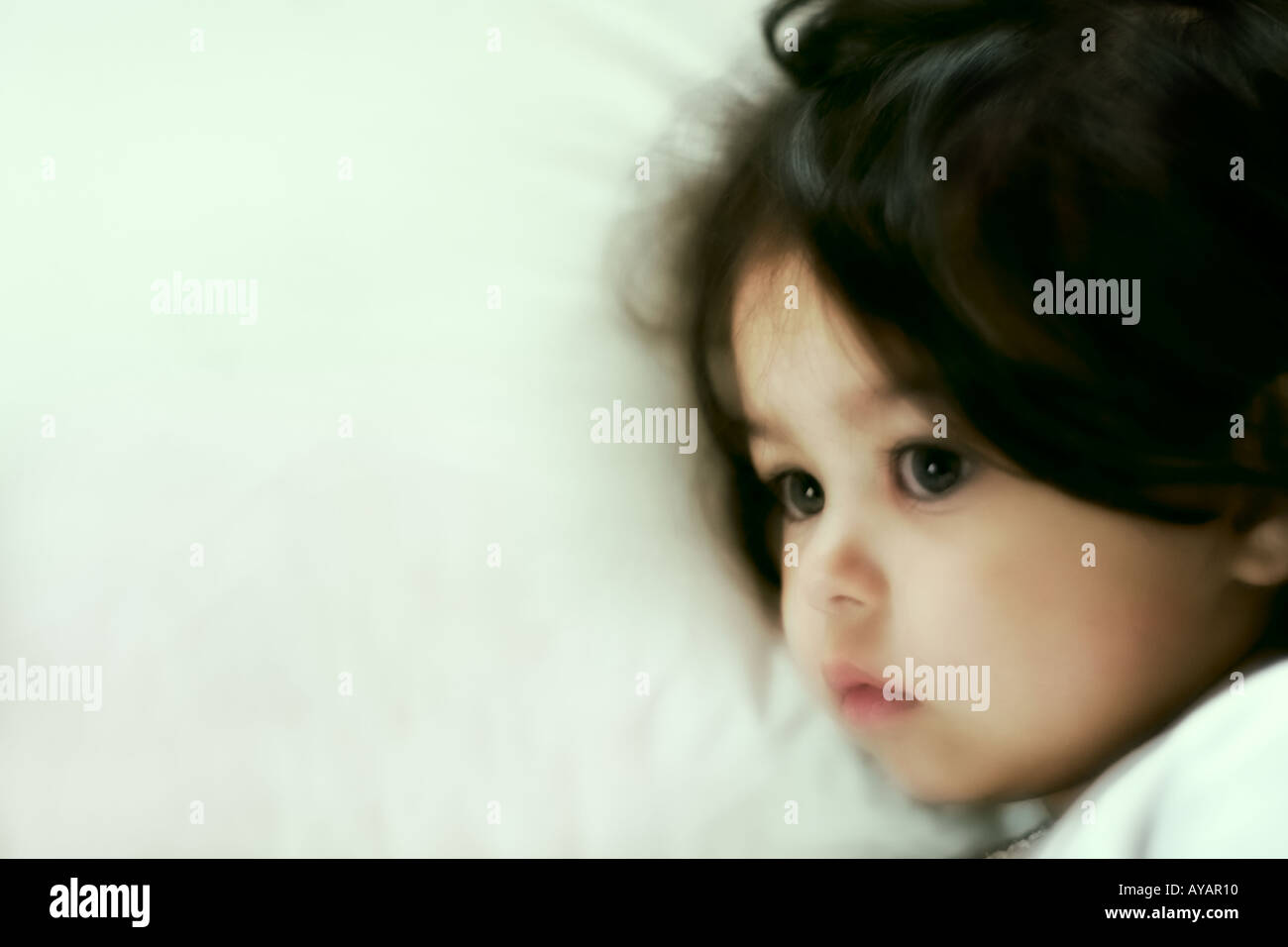 Little girl lying in bed in deep thought Stock Photo