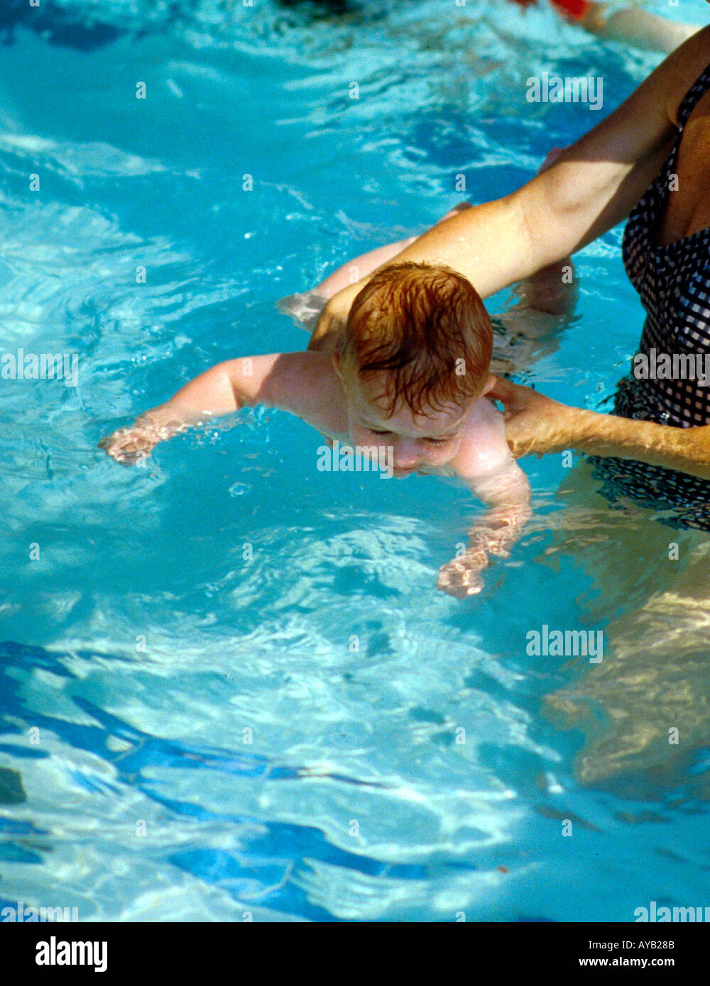 Young baby experiences the  feeling of water and learning to swim. Stock Photo