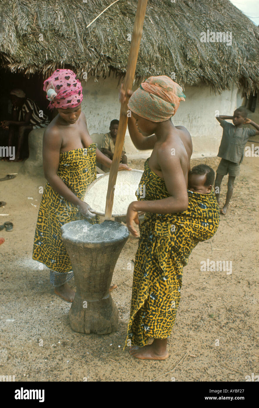 West Africa Liberia Kpelle tribe Women pounding manioc using mortar and pestle Woman is carrying her baby strapped on her back Stock Photo