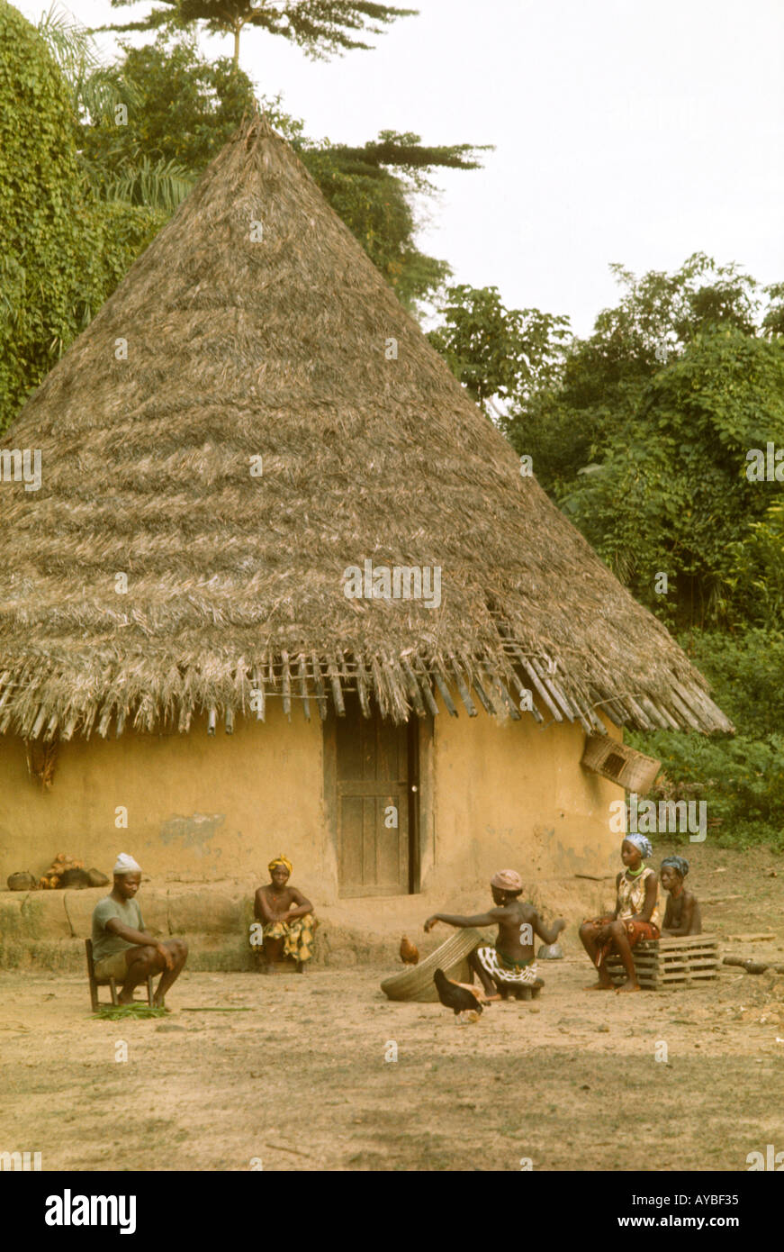 Africa Liberia Kpelle tribe village scene traditional cylindrical wattle and daub hut with conical thatch roof Woman is making a fishing net Stock Photo