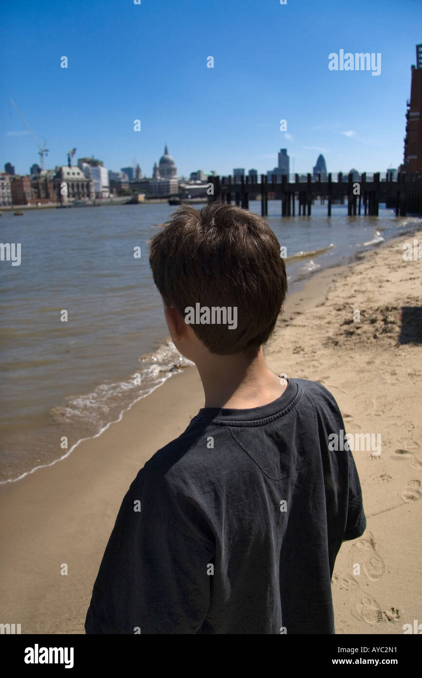 back view of a boy looking across the River Thames in London at the City on the opposite bank of the river Stock Photo