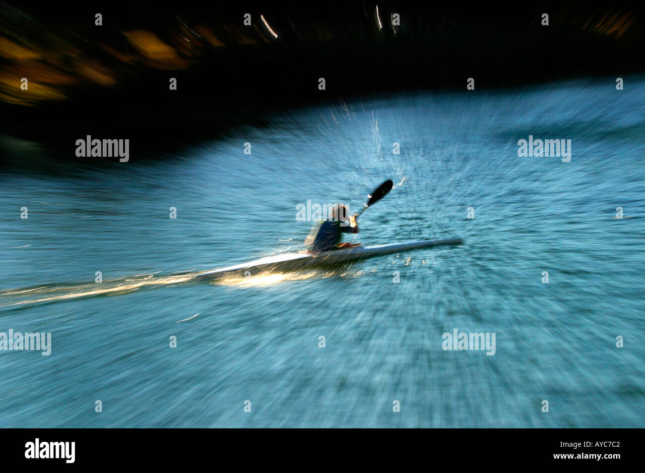 A canoeist paddling at speed through blue water in afternoon Stock
