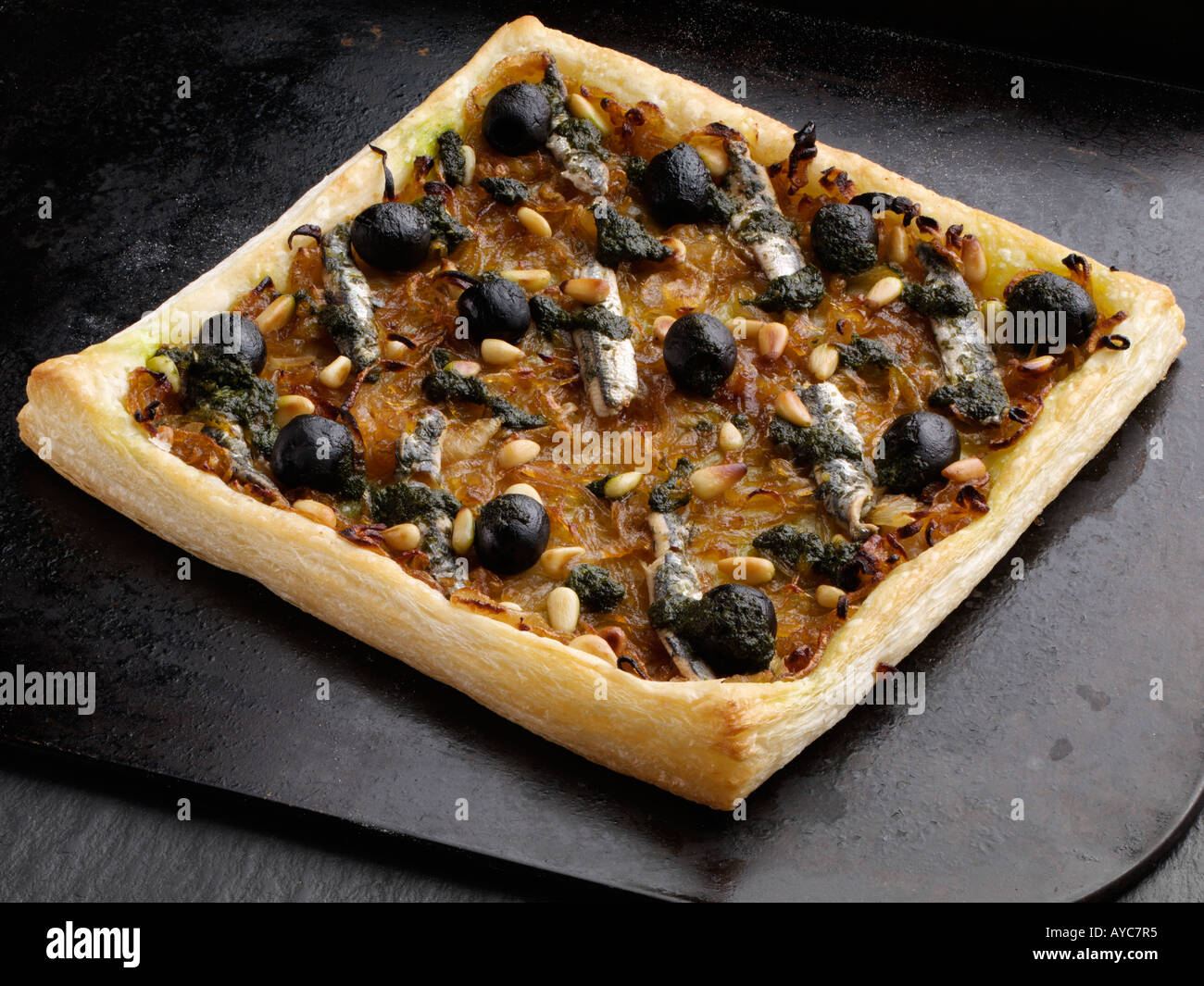 A whole pissaladiere pizza with black olives anchovies and pine nuts on