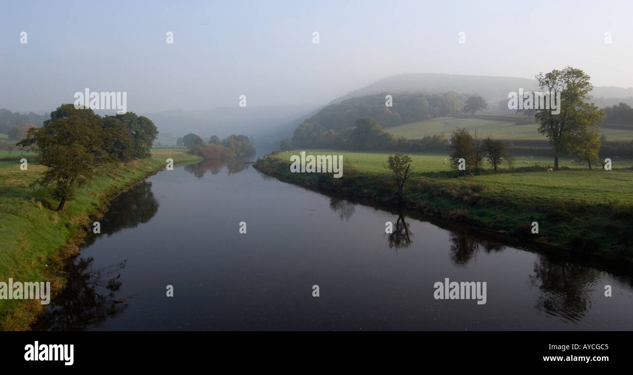 Beautiful tranquil river flowing through autumn countryside in early morning sun and mist Stock Photo