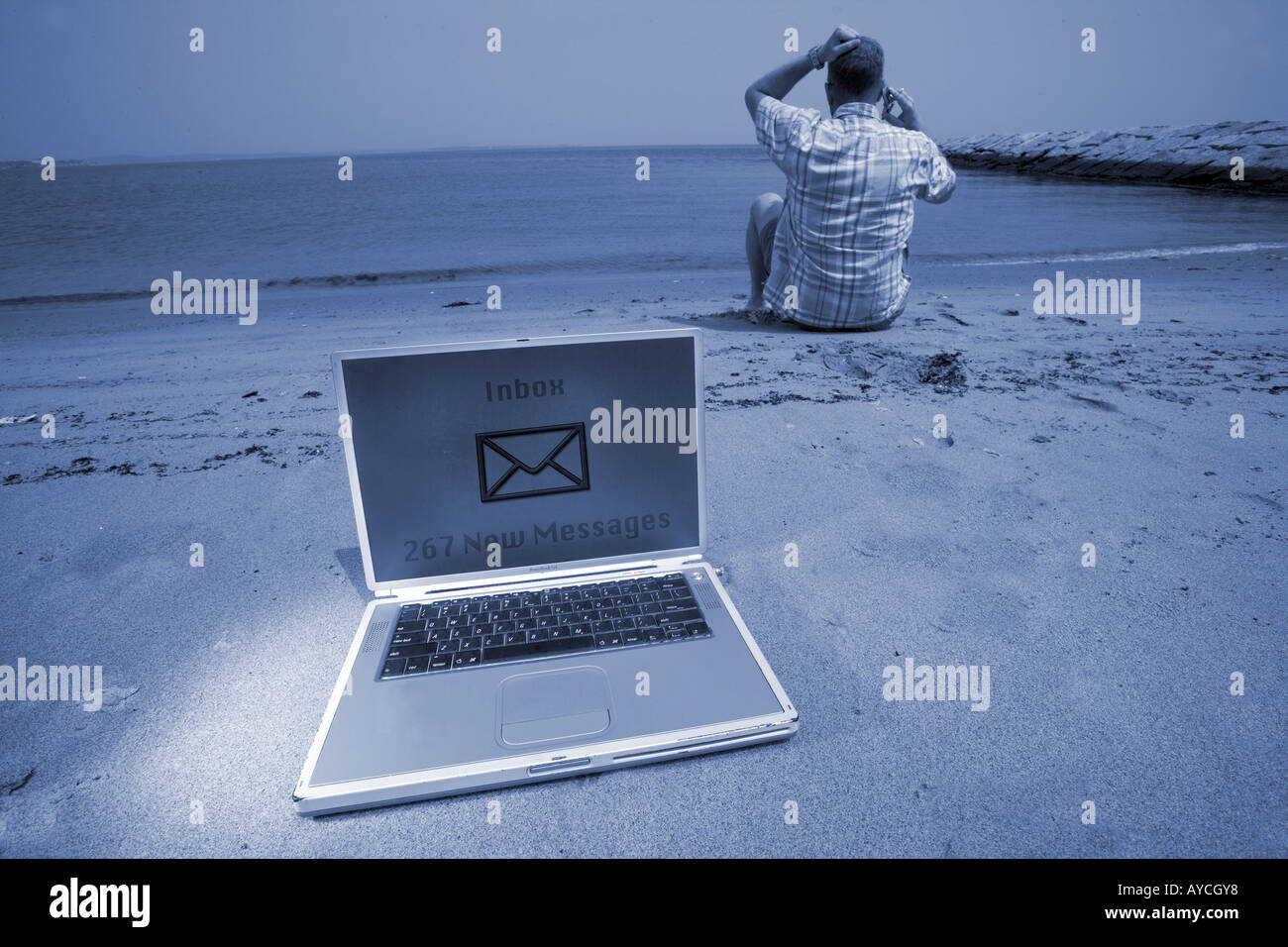 Man returning calls overworked on beach with cell phone and laptop on vacation Stock Photo