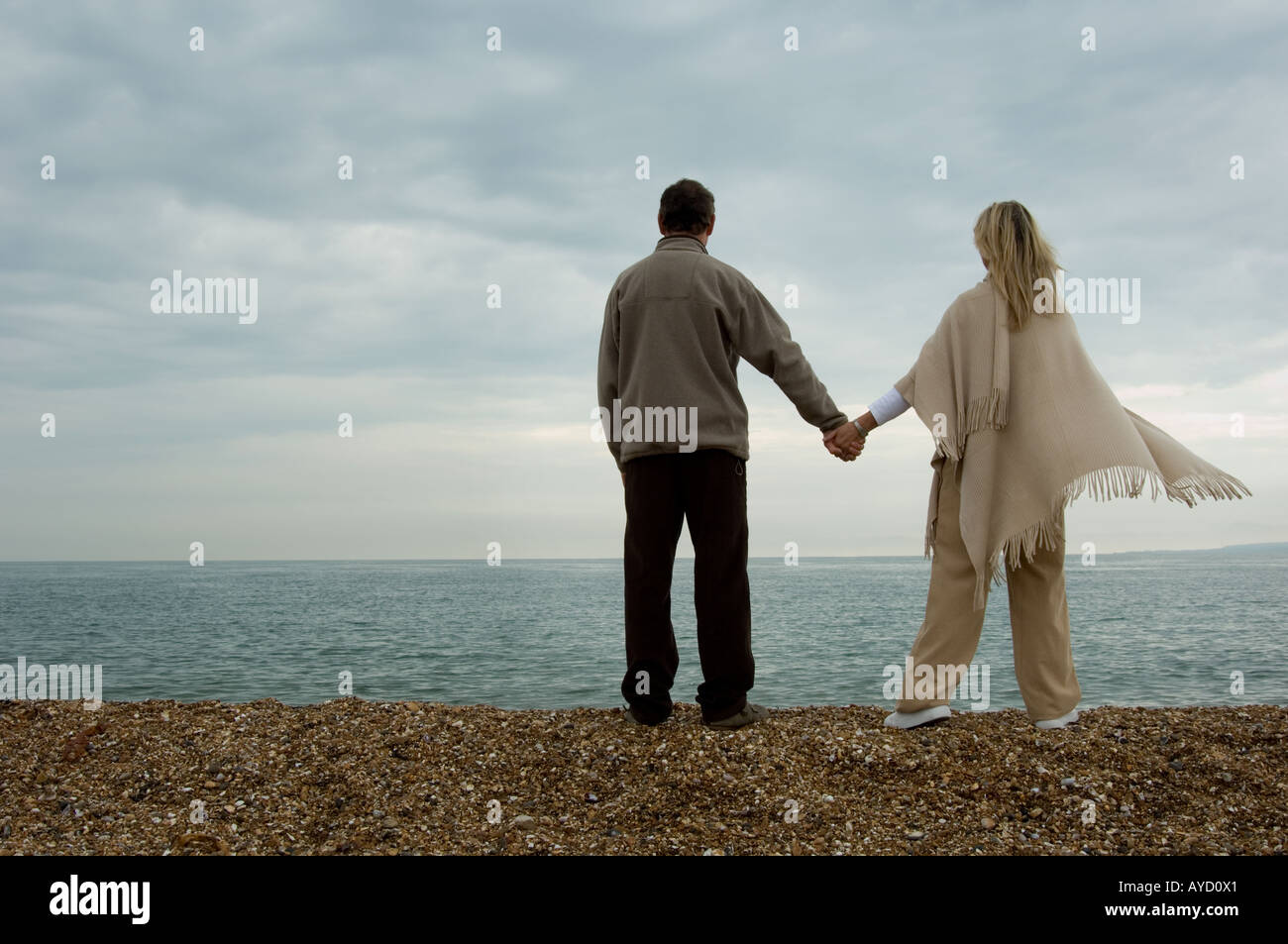 couple holding hands on beach looking out to sea Stock Photo - Alamy