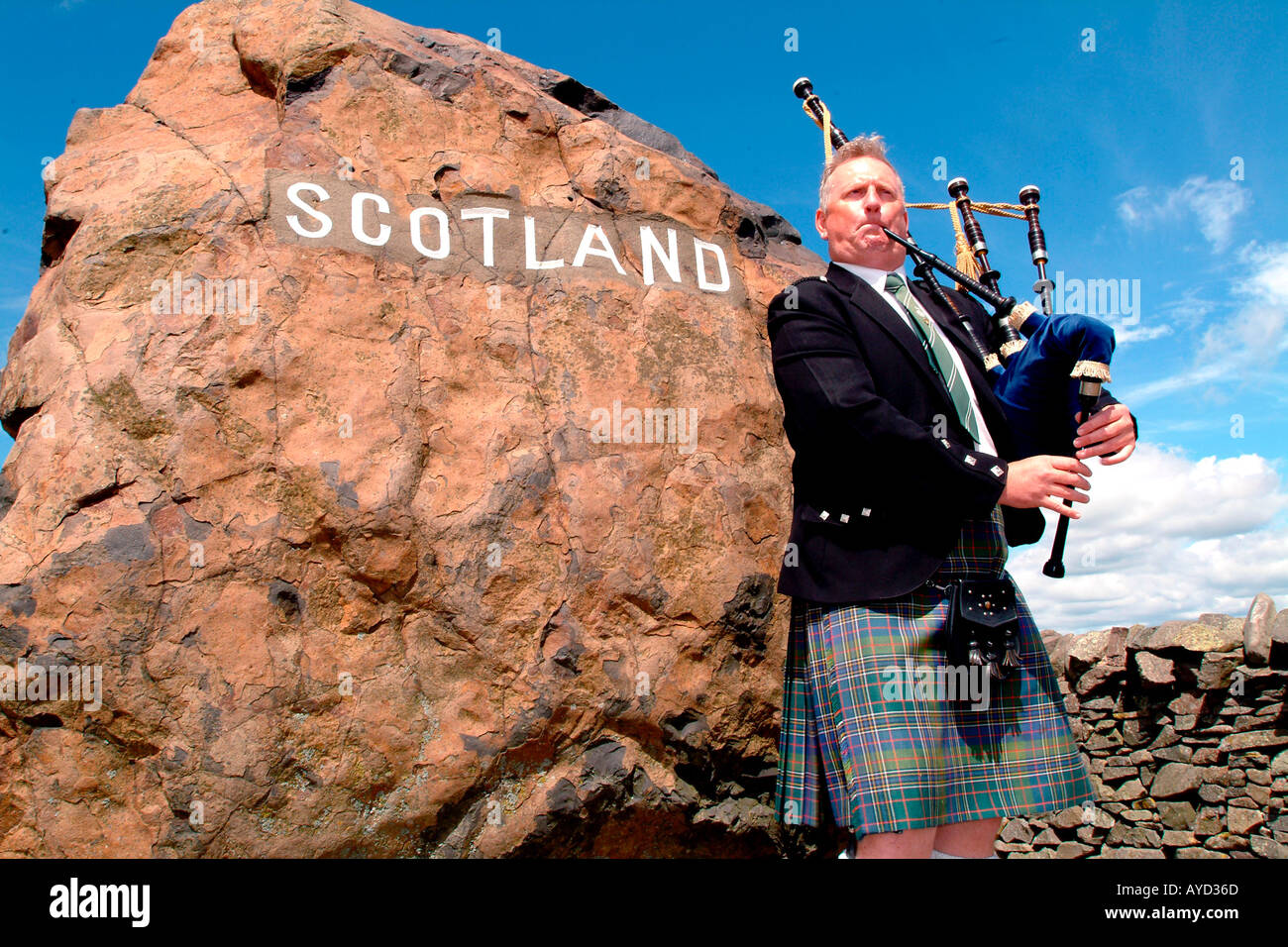 Scotsman playing the bagpipes at the England Scotland border sign Stock