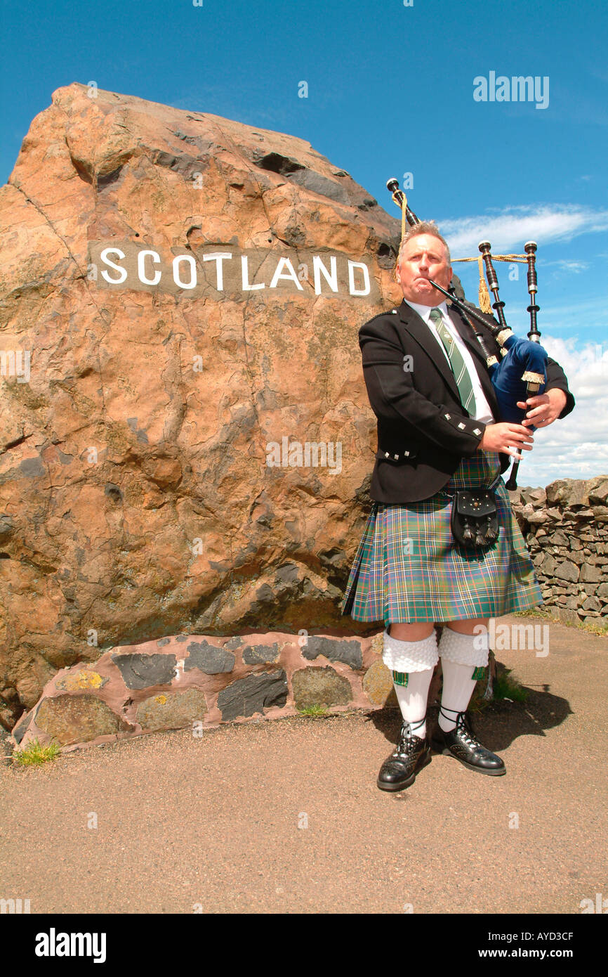 Scotsman playing the bagpipes at the England Scotland border sign Stock