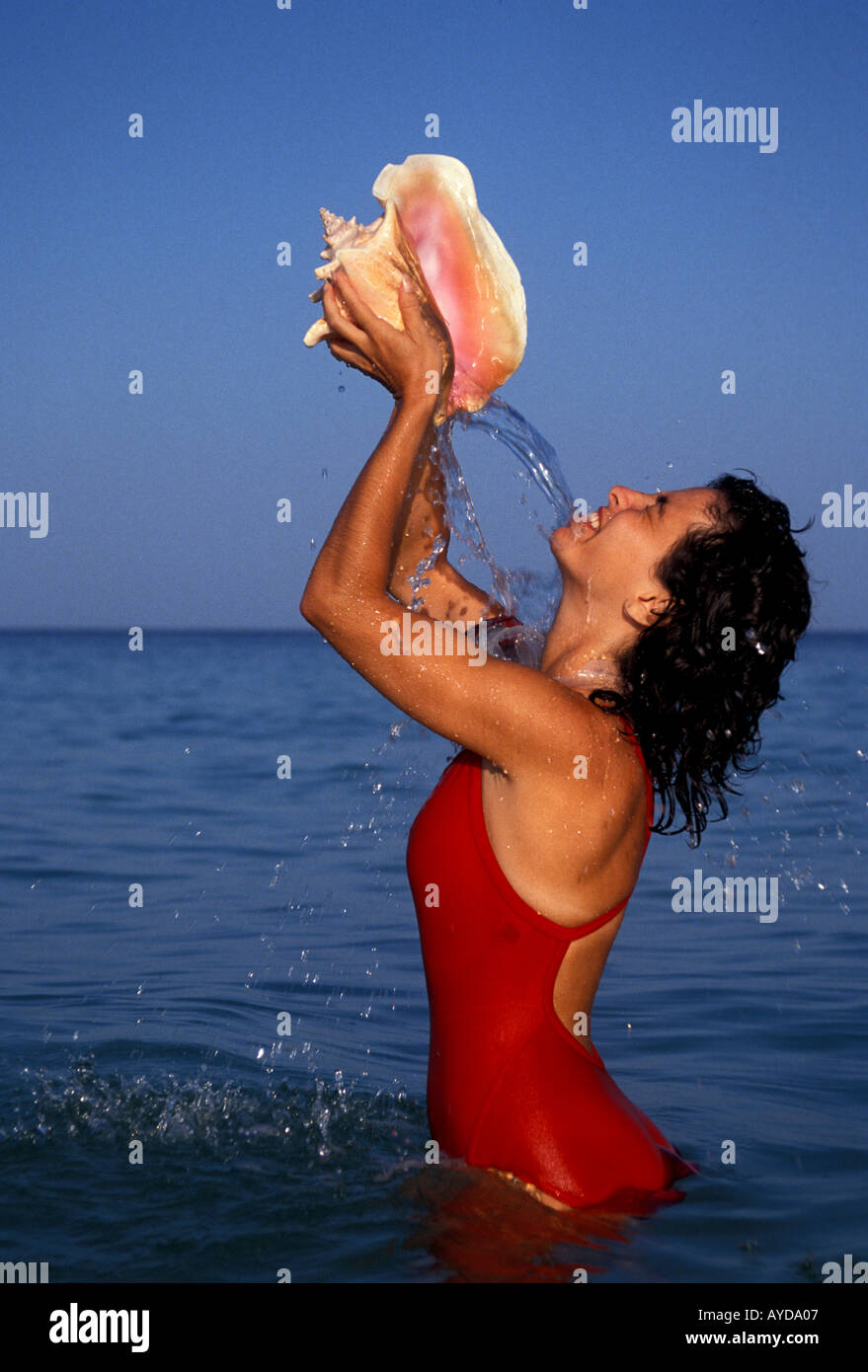 Caribbean woman holding conch shell and pouring water on self Stock Photo