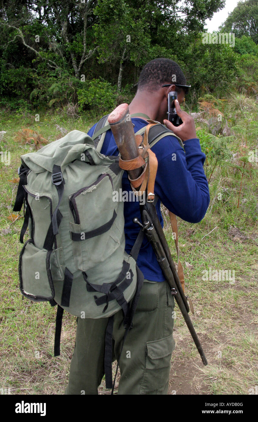 A game park wildlife ranger with a gun talks on his mobile phone Stock Photo