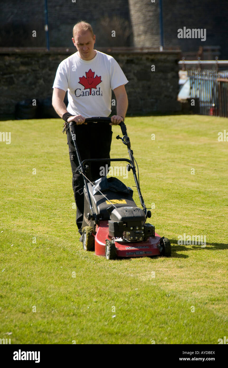 A Man wearing white tshirt mowing lawn in the sunshine, employed